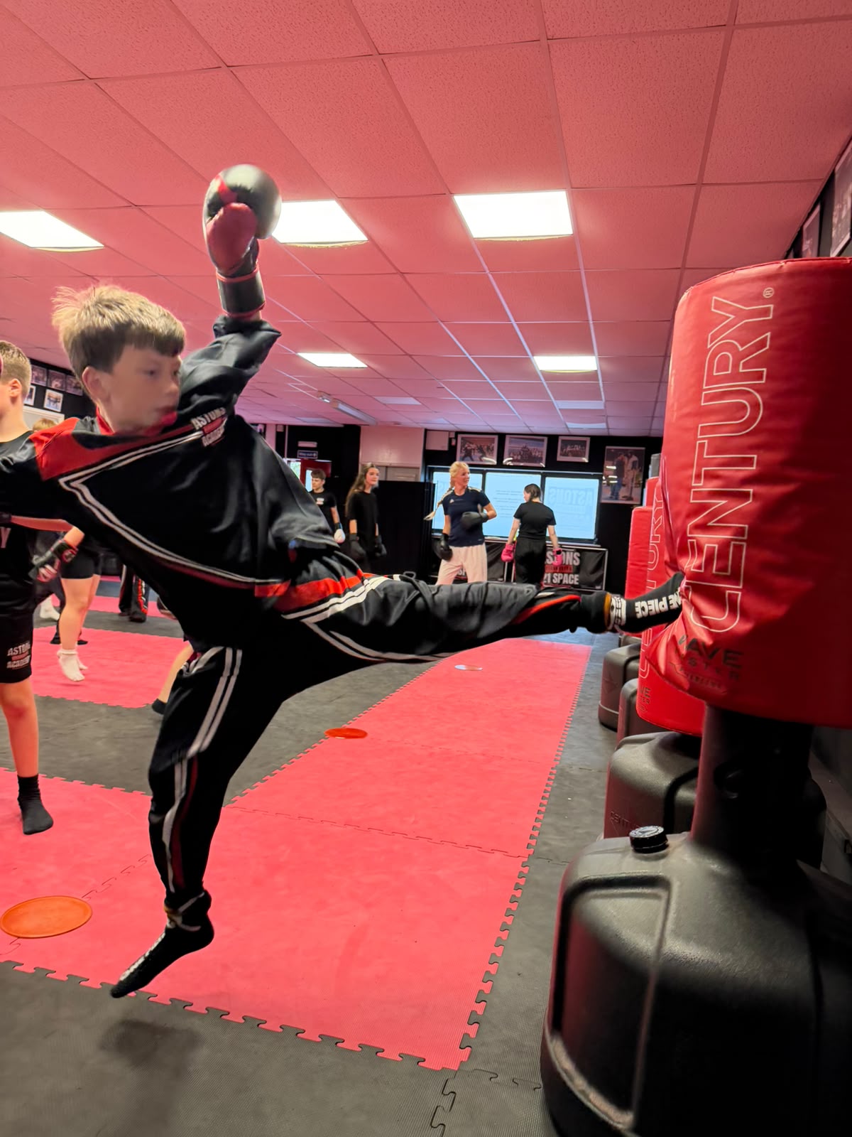 Boy landing a flying kick on a punching bag in class at Astons Kickboxing Academy, Shrewsbury