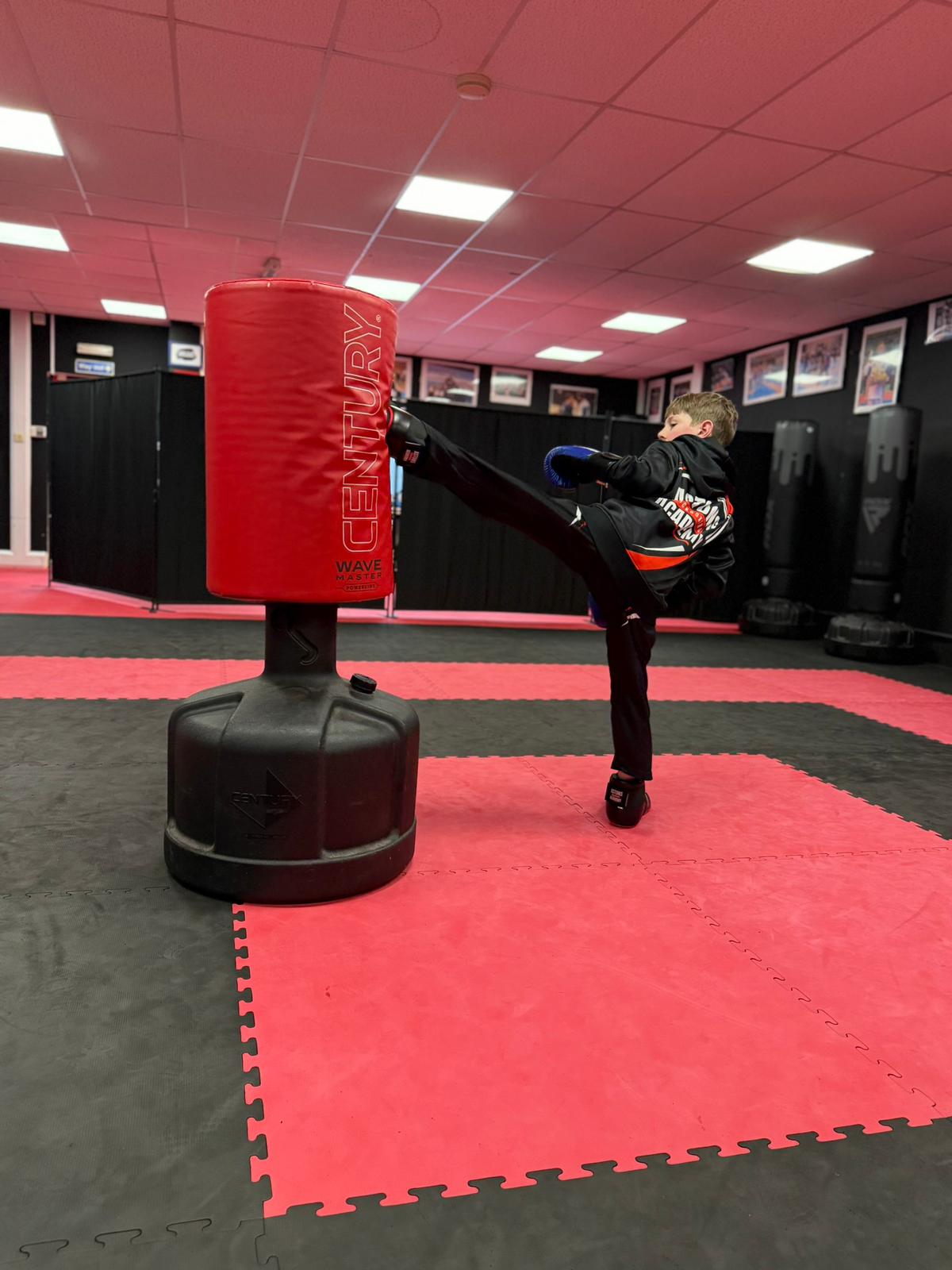Boy landing a high kick on a punching bag in kids kickboxing class at Astons Kickboxing Academy, Shrewsbury