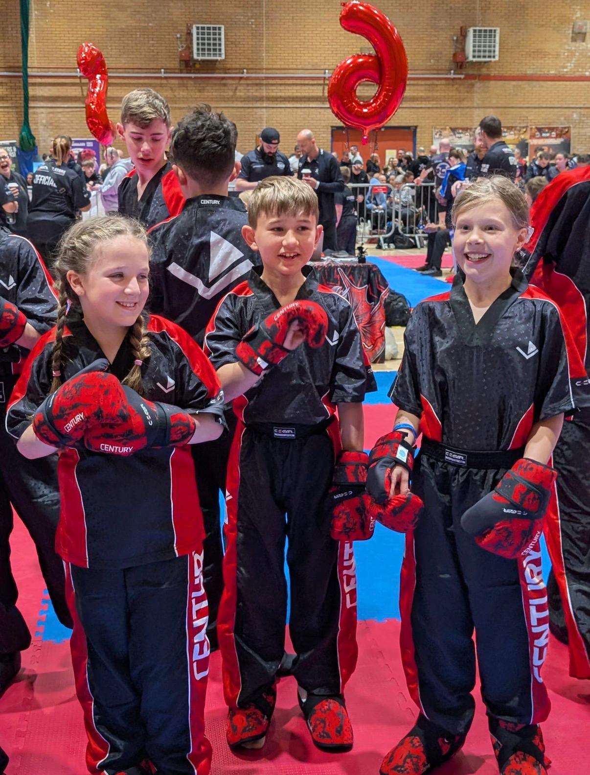 Three young Astons kickboxers celebrating with medals at a competition
